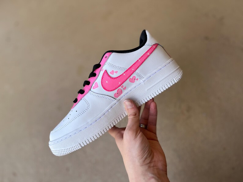 May include: White low-top sneakers with a pink swoosh and pink hearts on the side.