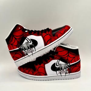 Puede incluir: Un par de zapatillas altas con tem&aacute;tica de Spider-Man. Los zapatos presentan un dise&ntilde;o de telara&ntilde;a roja y negra, detalles en blanco y un logotipo de Spider-Man. Las suelas son blancas y los cordones negros.