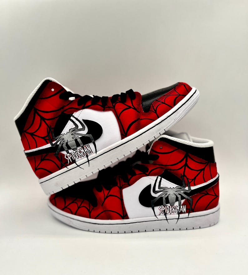Puede incluir: Un par de zapatillas altas con tem&aacute;tica de Spider-Man. Los zapatos presentan un dise&ntilde;o de telara&ntilde;a roja y negra, detalles en blanco y un logotipo de Spider-Man. Las suelas son blancas y los cordones negros.