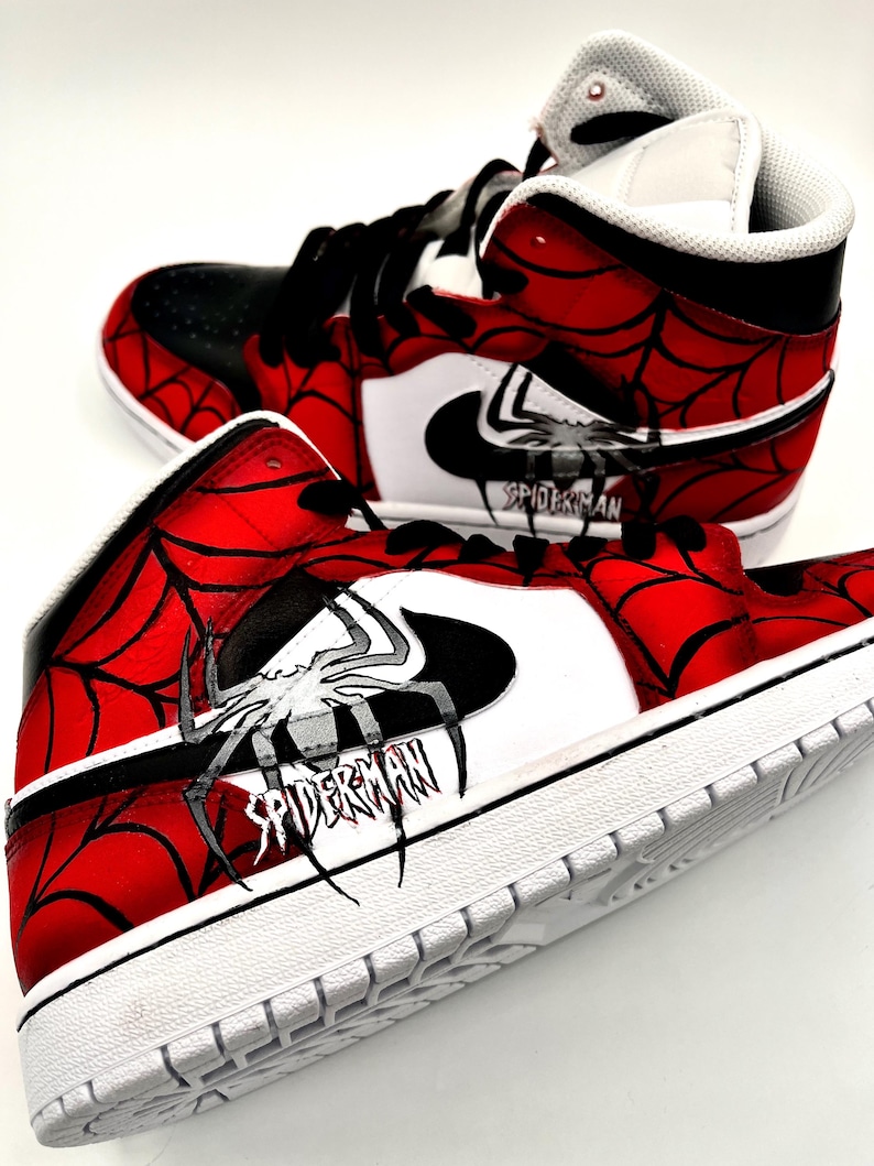 Puede incluir: Par de zapatillas altas con tem&aacute;tica de Spider-Man. Los zapatos presentan una combinaci&oacute;n de colores rojo y negro con un dise&ntilde;o de telara&ntilde;a. El logo de Nike es blanco y la palabra "SPIDERMAN" est&aacute; impresa en el lateral.