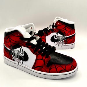 Puede incluir: Un par de zapatillas altas con tem&aacute;tica de Spider-Man. Los zapatos presentan un dise&ntilde;o de telara&ntilde;a roja y negra, detalles en blanco y el logotipo de Spider-Man. Las zapatillas tienen cordones negros y suela blanca.