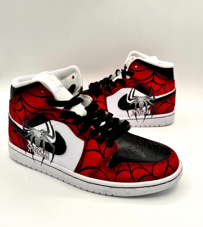 Puede incluir: Un par de zapatillas altas con tem&aacute;tica de Spider-Man. Los zapatos presentan un dise&ntilde;o de telara&ntilde;a roja y negra, detalles en blanco y el logotipo de Spider-Man. Las zapatillas tienen cordones negros y suela blanca.