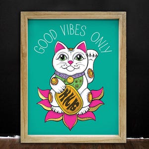 May include: A white cat with a pink flower behind it. The cat is holding a gold coin with the word "good" on it. The text "Good Vibes Only" is written in white on a teal background.