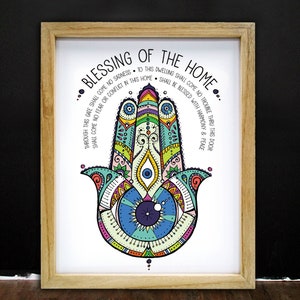 May include: A framed print featuring a colorful Hamsa hand design with intricate patterns in shades of blue, green, yellow, and pink. The text "BLESSING OF THE HOME" is at the top, with additional text around the hand. The frame is made of light-colored wood.