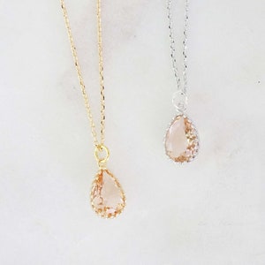 May include: Two necklaces with teardrop-shaped pendants. One has a gold chain and pendant setting, the other a silver chain and setting. The pendants are a light peach color and have a textured, faceted appearance.