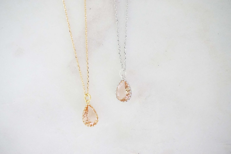 May include: Two necklaces with teardrop-shaped pendants. One has a gold chain and pendant setting, the other a silver chain and setting. The pendants are a light peach color and have a textured, faceted appearance.