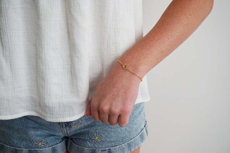 May include: A gold chain bracelet with a small, circular charm. The charm has a textured, sun-like design.