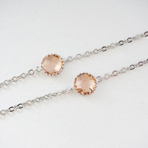 May include: Two delicate silver chains with a peach-colored crystal on each. The chains are linked together and the crystals are set in a silver bezel.