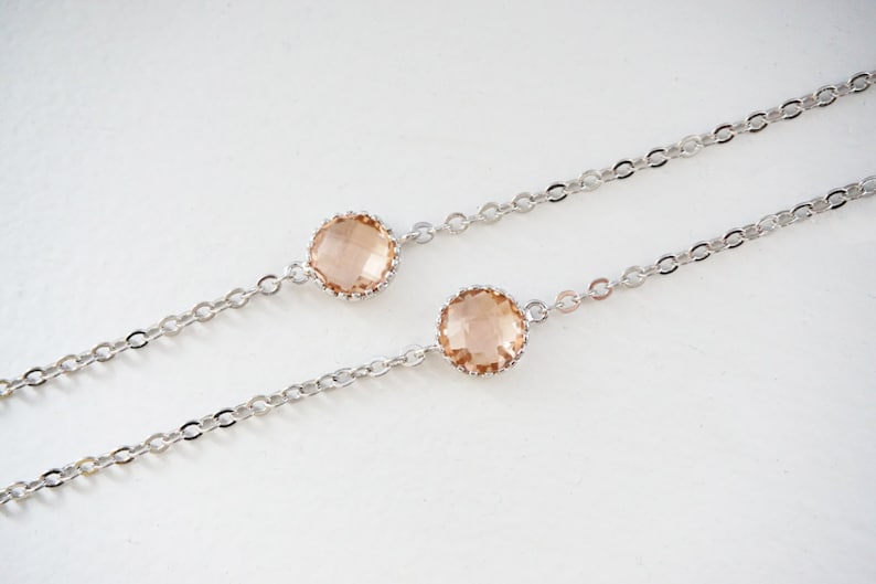 May include: Two delicate silver chains with a peach-colored crystal on each. The chains are linked together and the crystals are set in a silver bezel.