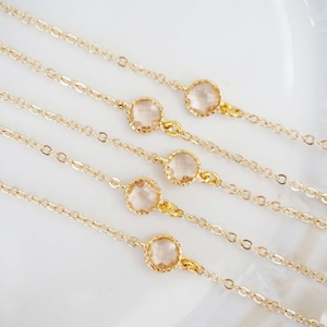 May include: Five delicate gold chains with a single clear crystal pendant on each. The chains are layered on a white surface.