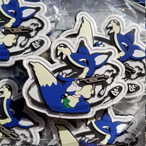 May include: Multiple blue and white embroidered patches featuring a cartoon fox holding a gun. The fox is wearing blue pants and a white shirt. The patches are packaged in clear plastic bags.