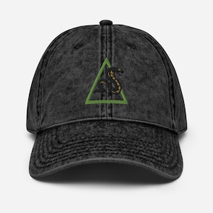 Peut inclure: Casquette de baseball noire avec un effet vieilli. Elle présente un motif brodé d'un serpent dans un triangle vert. Le serpent est détaillé en jaune et noir. La casquette a une visière incurvée et une sangle réglable.