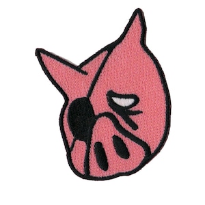 May include: Pink pig face with a black eye patch and a frowning expression. The pig is embroidered on a fabric patch.