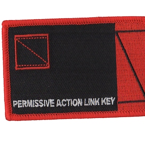 May include: Red and black fabric patch with white stitching. The patch has a diagonal line in a square on the left side and a diagonal line in a triangle on the right side. The text "PERMISSIVE ACTION LINK KEY" is printed in white below the design.