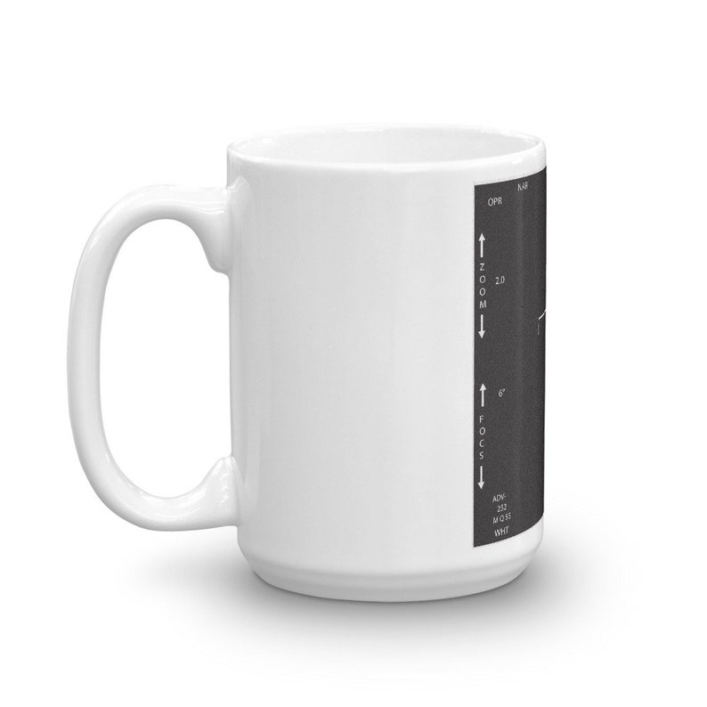 May include: White ceramic mug with a black and white image of a camera control panel on the side. The panel shows zoom and focus controls with the text "ZOOM", "FOCUS", "NOW", "2.0", "6", "252", "M 0.35", and "WHT".