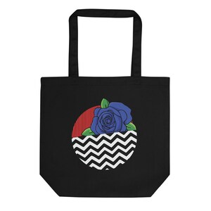 Puede incluir: Bolsa de tela negra con un patrón de chevron blanco y negro, una franja roja y una rosa azul en el centro.