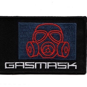 Pode incluir: Etiqueta bordada preta com um design de máscara de gás vermelha e o texto "GASMASK" em branco.