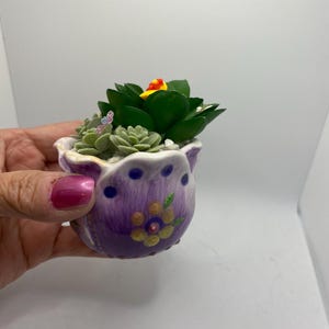 May include: A small purple ceramic planter with a floral design, filled with a succulent plant and decorative accents.