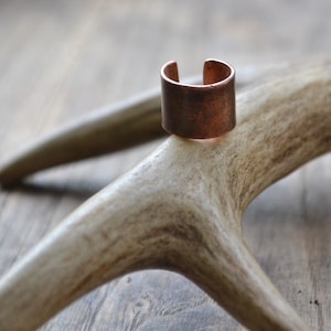 May include: A copper ring with a simple, rounded design. The ring is sitting on a piece of antler.