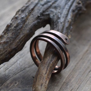 May include: A copper ring with a twisted design. The ring is made of two bands of copper that are twisted together. The ring is shown on a piece of wood.