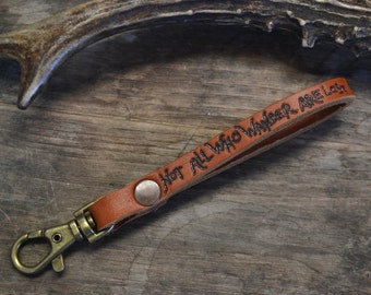 May include: A brown leather keychain with a silver key ring and the inscription "Not all who wander are lost".