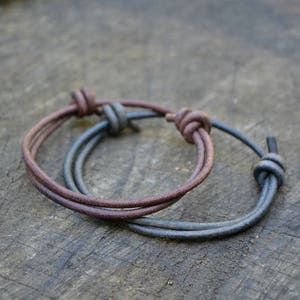 May include: Two leather bracelets, one brown and one black, tied together with a knot.