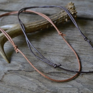 May include: Two leather cords, one brown and one dark brown, are tied in knots and laid out on a wooden surface.