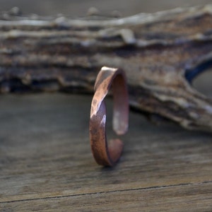 May include: A hammered copper ring with a twisted design. The ring is on a wooden surface.