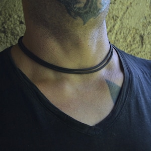Peut inclure: Gros plan d'une personne portant un collier ras du cou noir. Le collier est composé de deux fines cordes noires.