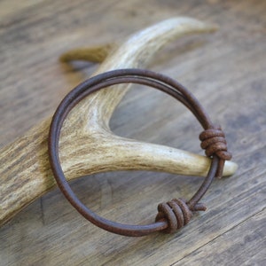 May include: A brown leather bracelet with two knotted ends. The bracelet is wrapped around a piece of antler.