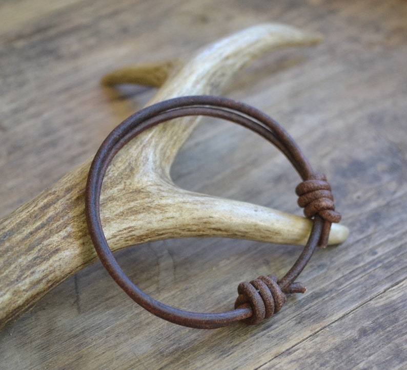 May include: A brown leather bracelet with two knotted ends. The bracelet is wrapped around a piece of antler.
