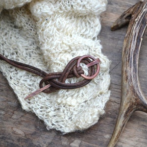 Pu&ograve; includere: Un cordoncino di cuoio marrone con un anello di rame e un'estremit&agrave; appuntita &egrave; legato in un nodo. Il cordoncino &egrave; avvolto attorno a un tessuto bianco e soffice e un corno di cervo marrone.