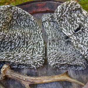 May include: Two knitted hats in a green and white pattern, lying on a wooden surface with a brown antler.