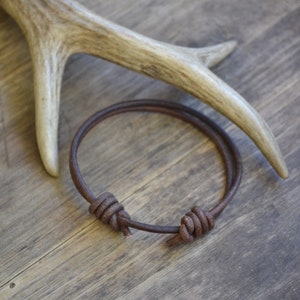 May include: A brown leather bracelet with two knots on a wooden surface.