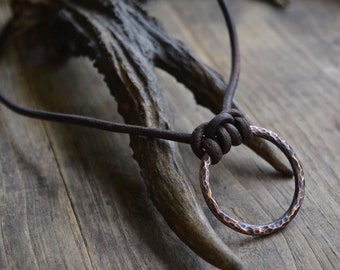 Può includere: Una collana in corda di cuoio marrone con un ciondolo rotondo in rame martellato.