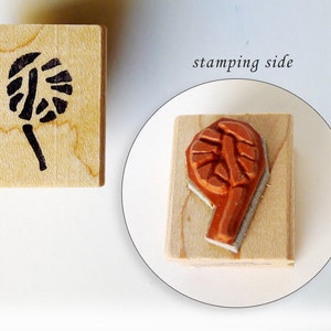 May include: Two wooden blocks with a design carved into them. The first block has a black design of a flower with a stem. The second block has a brown design of a flower with a stem. The text "stamping side" is written on the image.