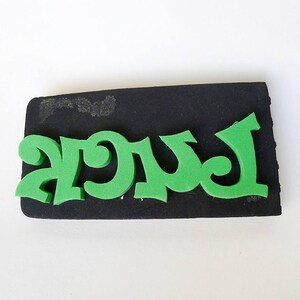 May include: Green foam letters spelling out the word "AGUA" on a black foam block.