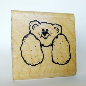 May include: A wooden rubber stamp with a black and white illustration of a teddy bear with a smiling face.