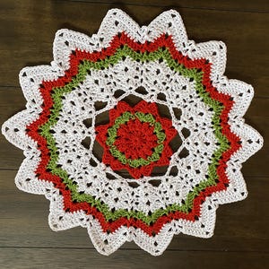 May include: White crochet doily with a red and green center. The doily has a starburst pattern and is perfect for adding a touch of handmade charm to your home decor.