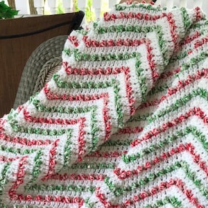 May include: A white crocheted blanket with red and green stripes. The blanket is folded and draped over a wicker chair.