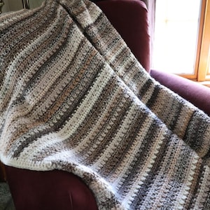 May include: A brown, beige and white striped crocheted throw blanket draped over a burgundy armchair.