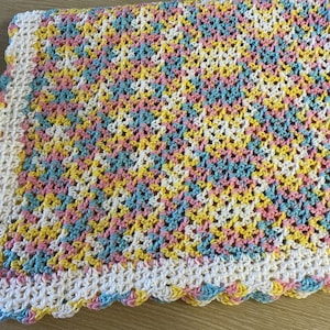 Könnte beinhalten: Eine gehäkelte Babydecke mit einem gewellten Rand in den Farben Rosa, Gelb, Blau und Weiß.
