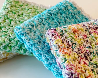 May include: A stack of four handmade crochet washcloths in various colors. The washcloths are in shades of yellow, green, blue, and a multicolored yarn with red, yellow, and purple. The crochet stitch creates a textured surface.