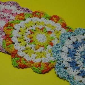 May include: Three crocheted dishcloths in different colors. The first is pink and white, the second is yellow, green, and orange, and the third is blue and white.