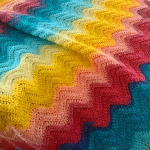 May include: A colourful crocheted blanket with a chevron pattern in shades of yellow, orange, pink, red, blue, and green.
