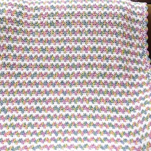 May include: A crocheted baby blanket with a white background and a colourful geometric pattern. The blanket has a scalloped edge.