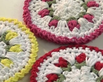 May include: Three handmade crochet coasters in a circular floral design. One coaster has a yellow border, another has a pink border, and the third has a red border. The coasters are white with pink, red, and green accents.