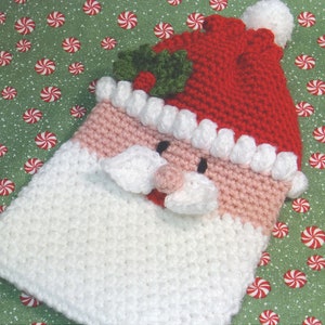 May include: Crocheted Santa Claus ornament with a white beard, pink cheeks, and a red hat with green holly.