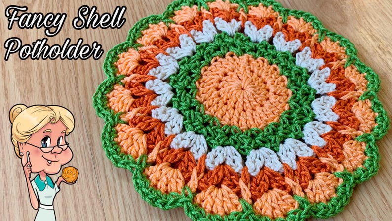 May include: A crocheted pot holder in the shape of a flower with orange, peach, white, and green yarn. The text "Fancy Shell Potholder" is visible in the image.