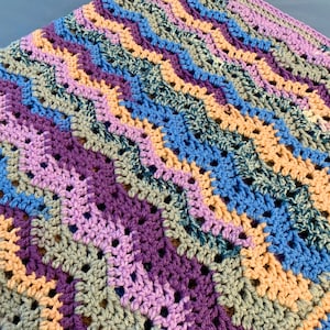May include: A crocheted blanket with a chevron pattern in shades of purple, blue, peach, and green.